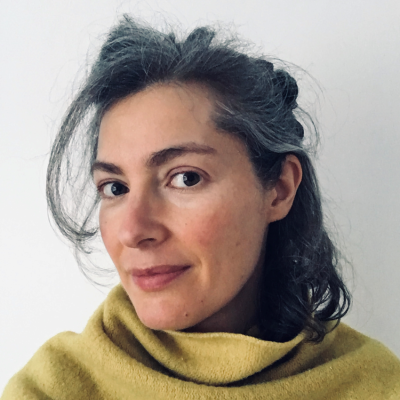 A white woman with dark hair and brown eyes wearing a yellow scarf